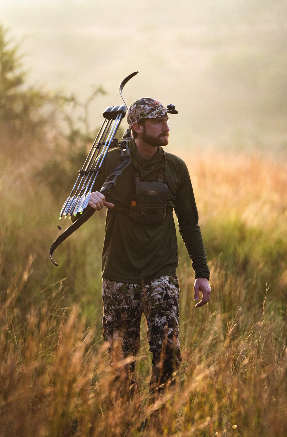 A hunter walking the field with a bow